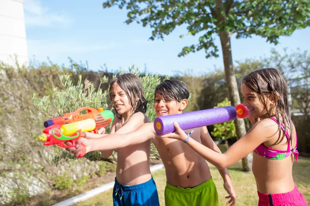 Niños jugando con pistolas de agua en verano, disfrutando de una actividad activa y refrescante al aire libre
