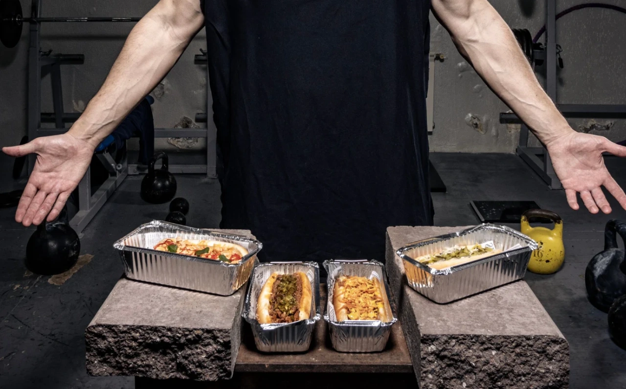 Hombre en un gimnasio mostrando varias comidas saludables preparadas para acompañar una rutina de entrenamiento