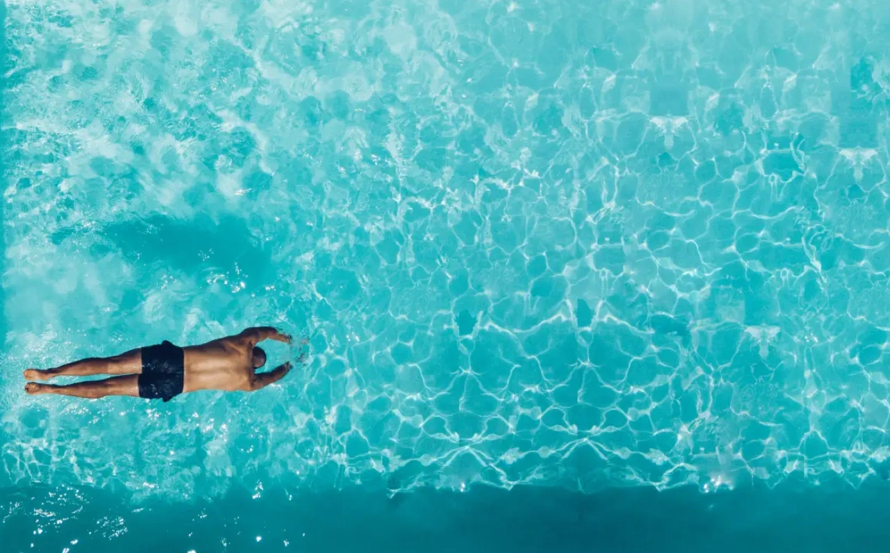Hombre lanzándose al agua en una piscina exterior para refrescarse en verano