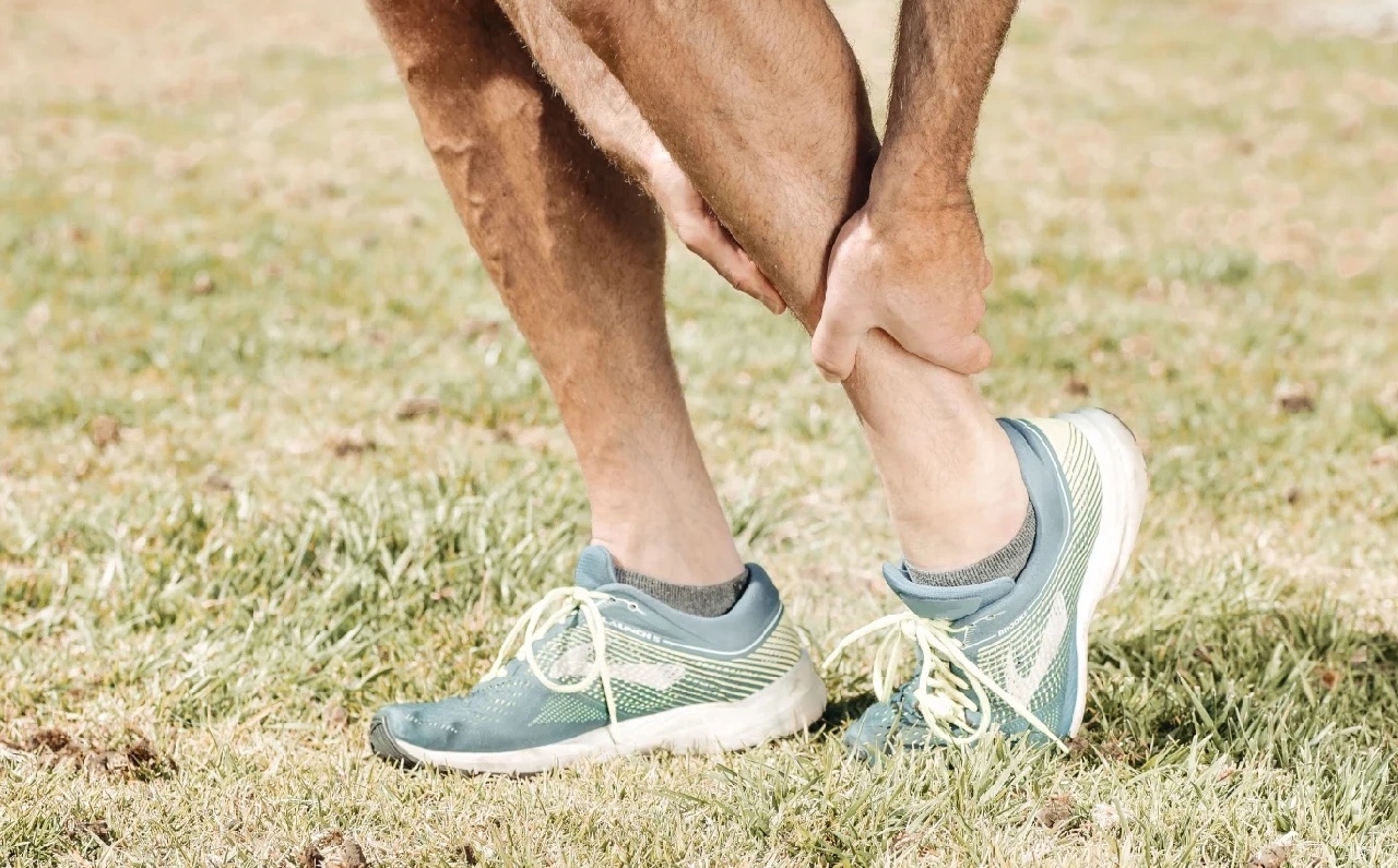 Un hombre sujetándose el tobillo tras notar una molestia, una señal de alerta que conviene no ignorar durante el entrenamiento.
