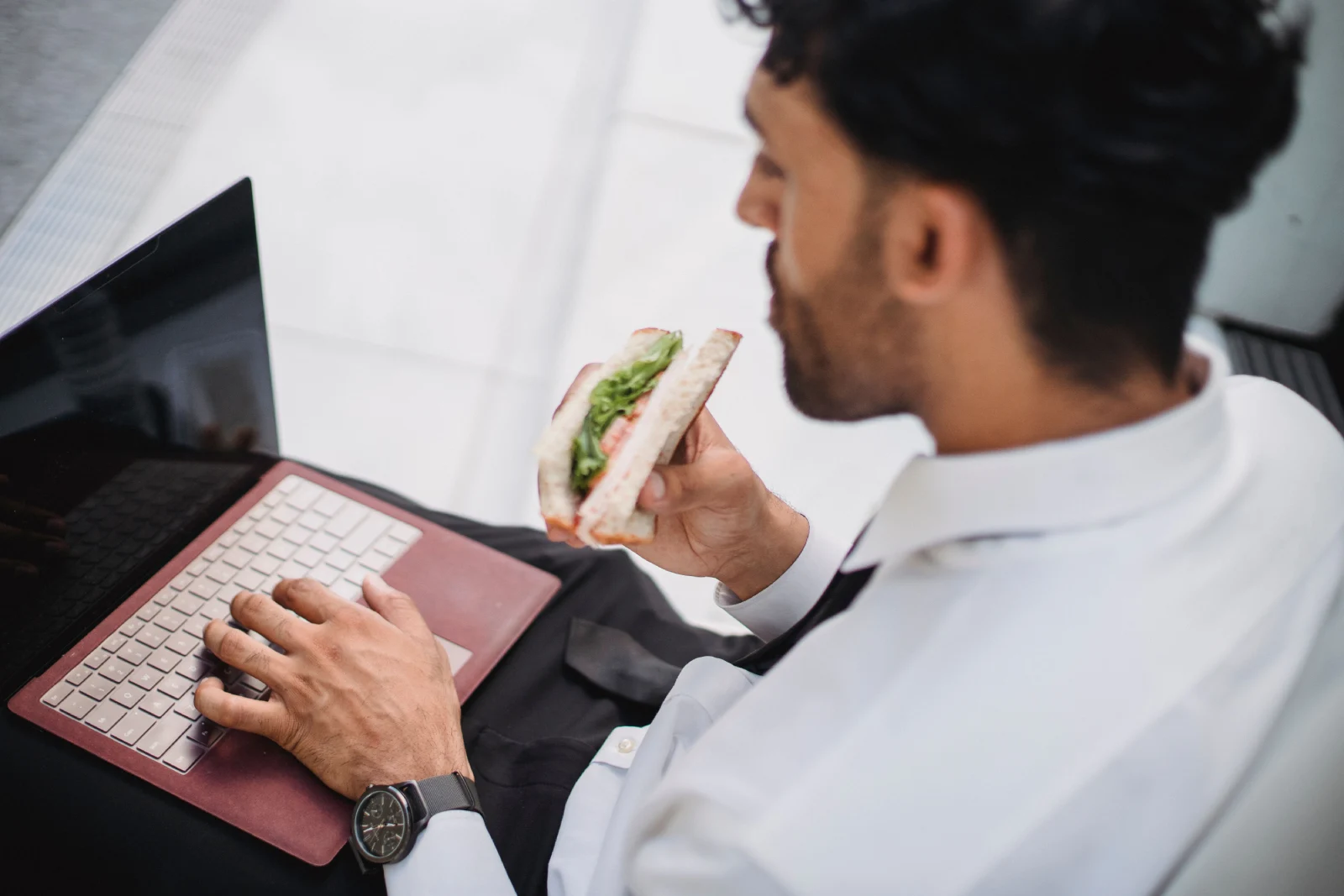Hombre comiendo un sándwich mientras trabaja con el ordenador durante la jornada laboral.