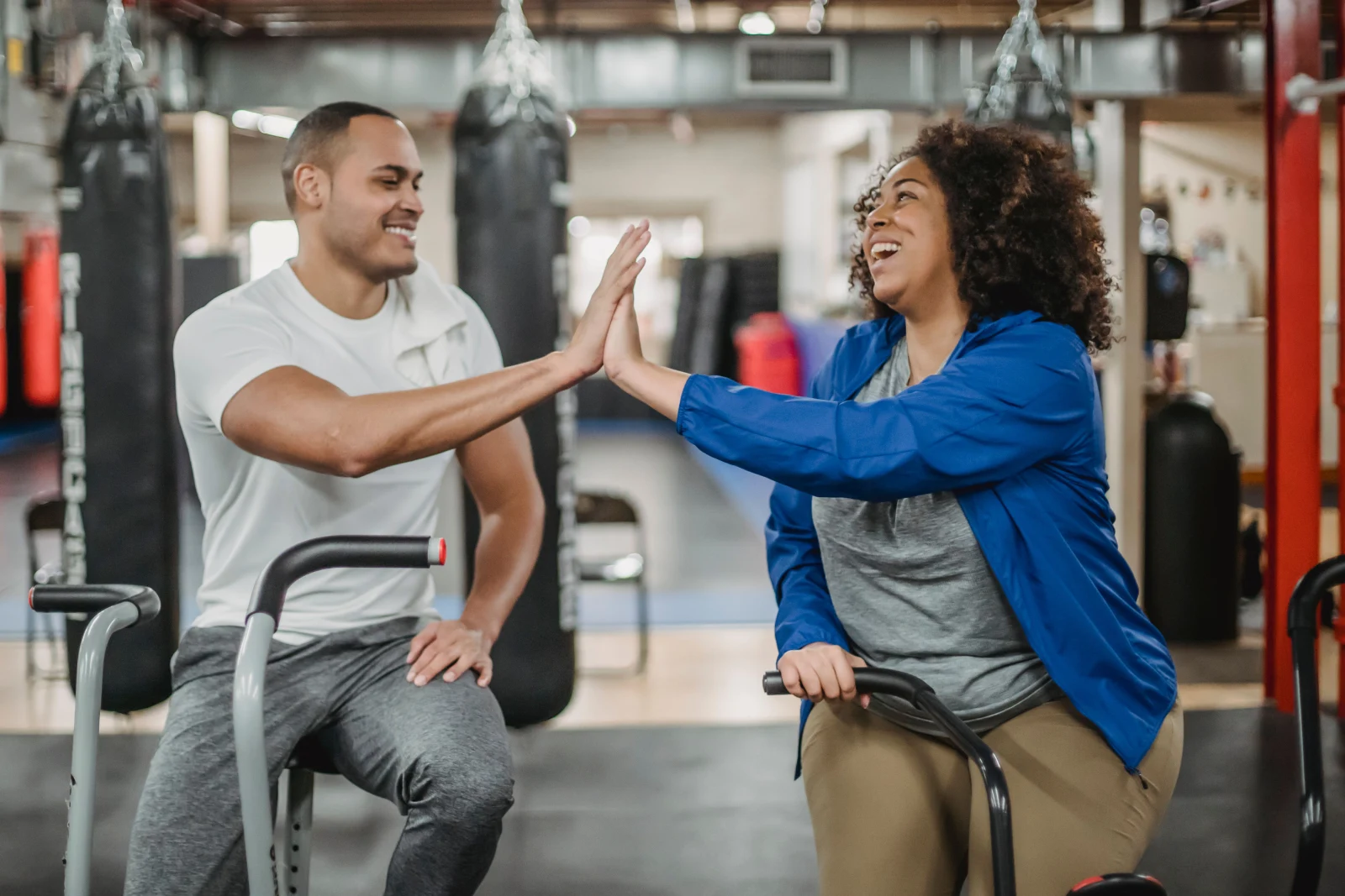 Dos personas se felicitan con un choque de manos tras entrenar en un gimnasio, reflejando motivación y bienestar.