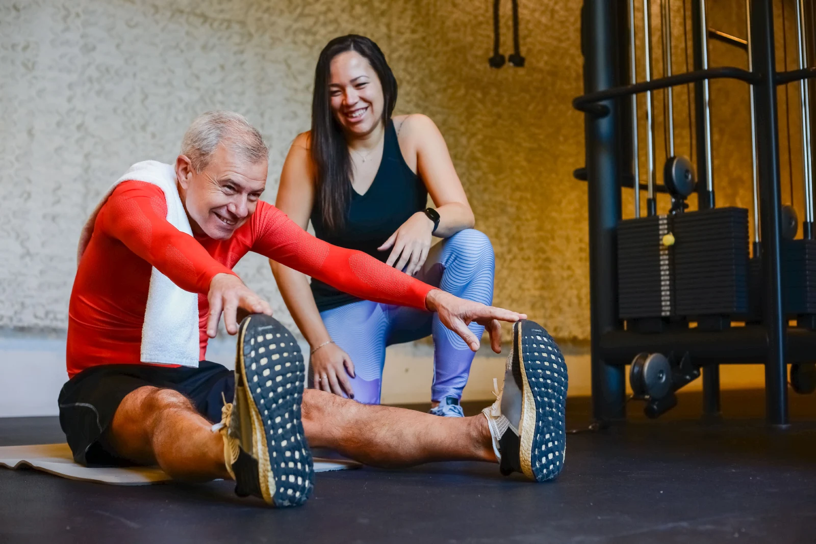 Entrenador acompaña a un hombre mayor durante un ejercicio de estiramiento en el gimnasio.