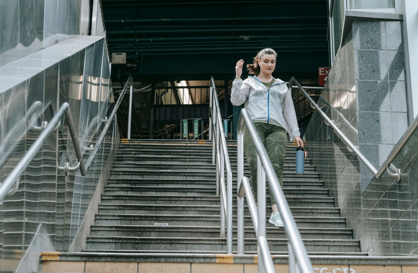 Mujer con ropa deportiva bajando unas escaleras con una botella de agua, preparada para retomar su rutina de entrenamiento.
